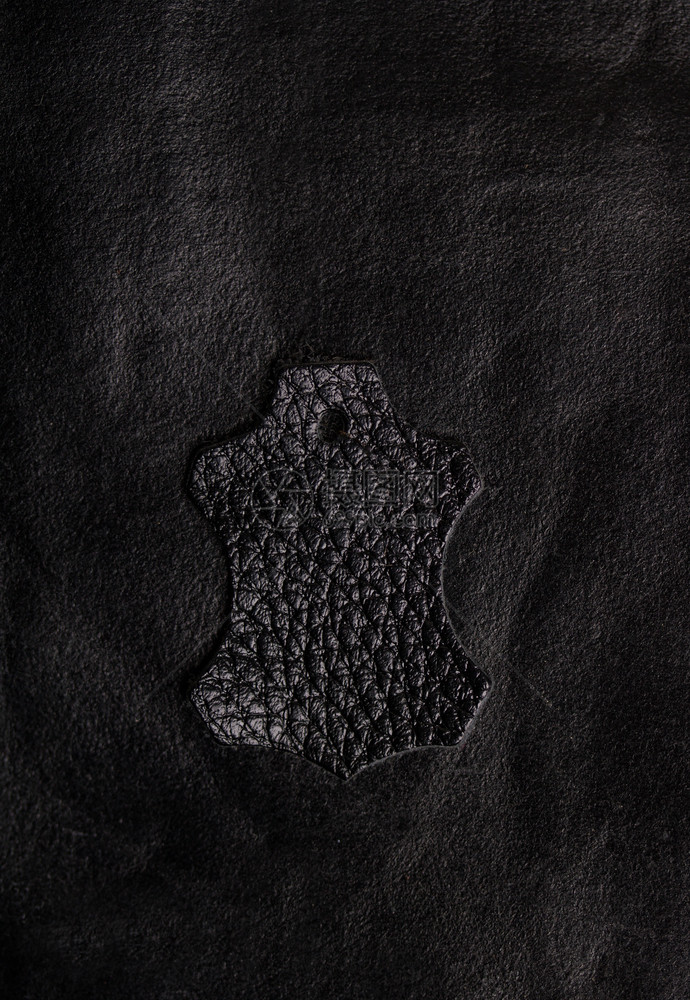 典型的皮革徽章位于粗糙的黑色皮革表面符号黑色图片