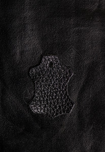 典型的皮革徽章位于粗糙的黑色皮革表面符号黑色图片