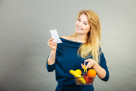幸福的妇女拿着水果购物篮看帐单享受低价图片