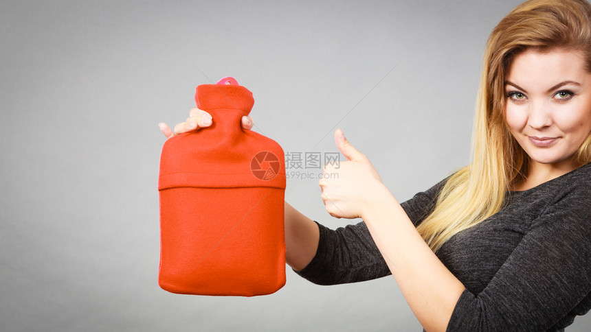 积极的微笑妇女建议用红色软羊毛罩灰的热水瓶医疗保健止痛药康复概念快乐妇女拿着热水瓶图片