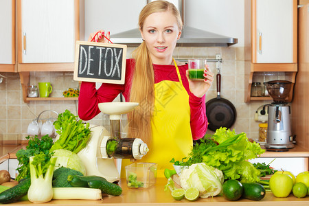 厨房的年轻女子在除毒标志旁边的玻璃杯中拿着绿色健康蔬菜冰淇淋汁图片