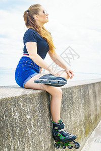 身穿溜冰鞋的年轻女子坐在海边休息背景图片