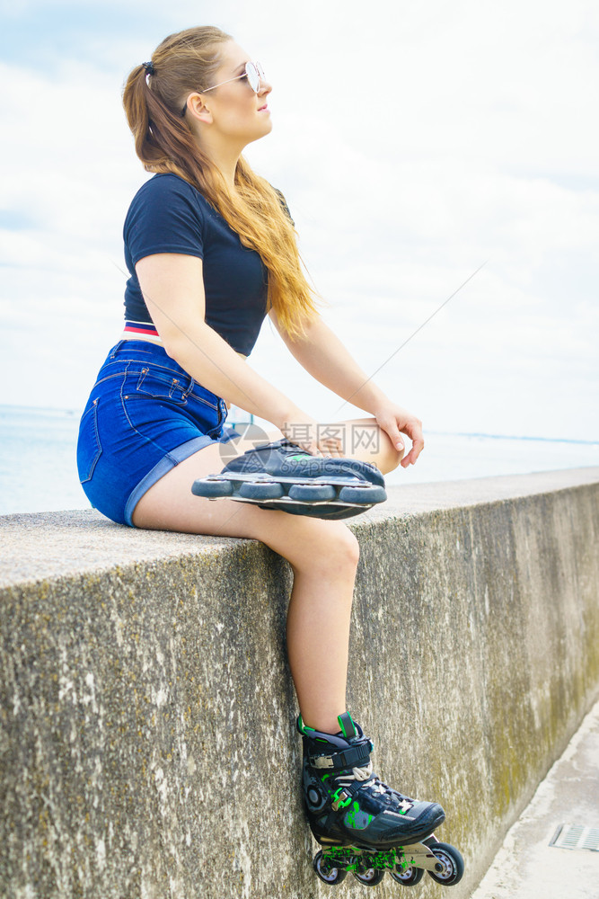 身穿溜冰鞋的年轻女子坐在海边休息图片