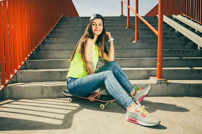 酷的长发少女坐在城市楼梯附近的滑板上夏天生活方式很滑稽特伦迪运动青少年有滑板的女孩在楼梯上图片
