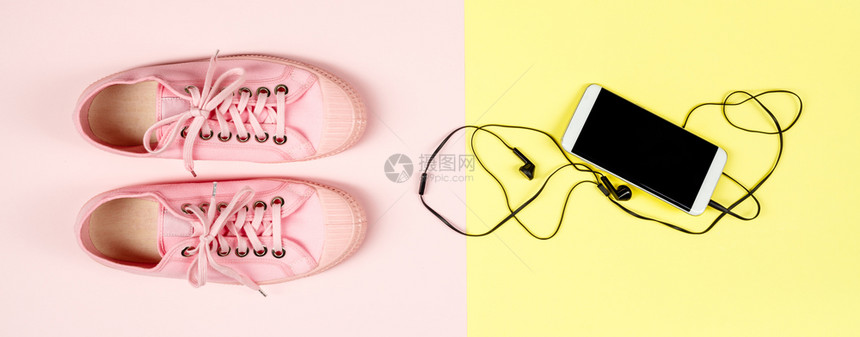 粉红背景的色帆布运动鞋和智能手机顶部平面风景时装女饰品生活方式或旅行概念粉色帆布运动鞋和移电话关闭图片