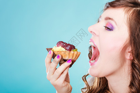 甜美的食物饱和脂肪的概念妇女面对张开的嘴吃蛋糕蓝背景背景图片