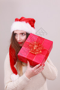 带着礼物的好奇女人拿着带丝盒戴圣塔帽的年轻女孩庆祝圣诞节的日放松概念图片