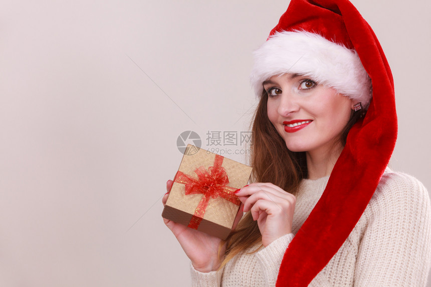 穿着圣达克萨斯帽子的快乐女人拿着红弓的金礼盒圣诞节时间赠与和幸福的概念拿着礼物盒的女人图片