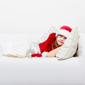 女孩在圣诞节时的家庭间可爱的小女人爬在沙发上小女人躺在沙发上休息时间穿着红色的圣达克萨斯帽子和鞋可爱的小女人爬在沙发上背景图片