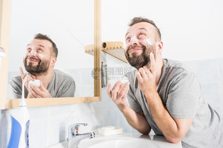 男人在浴室镜子前脸上涂满了香水男人在浴室里涂了润湿霜图片
