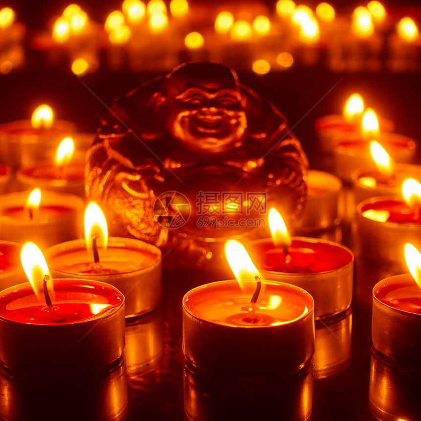 燃烧的蜡烛和幸运佛雕像集中关注前面的蜡烛图片