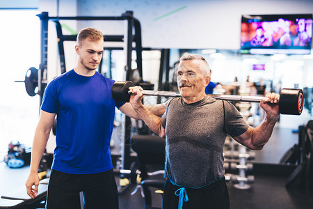 老年男子和健身房私人教练举重室内锻炼老年男子在健身房协助老年男子图片