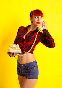 女孩穿一件明亮的格衬衫绑在肚子上短裤电话以亮黄色背景说话图片