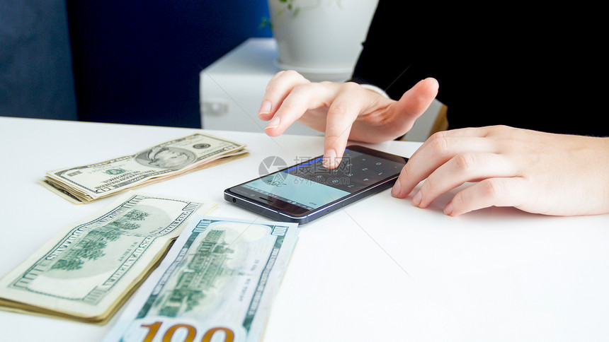 女银行家在计钱时使用智能手机的近视照片图片
