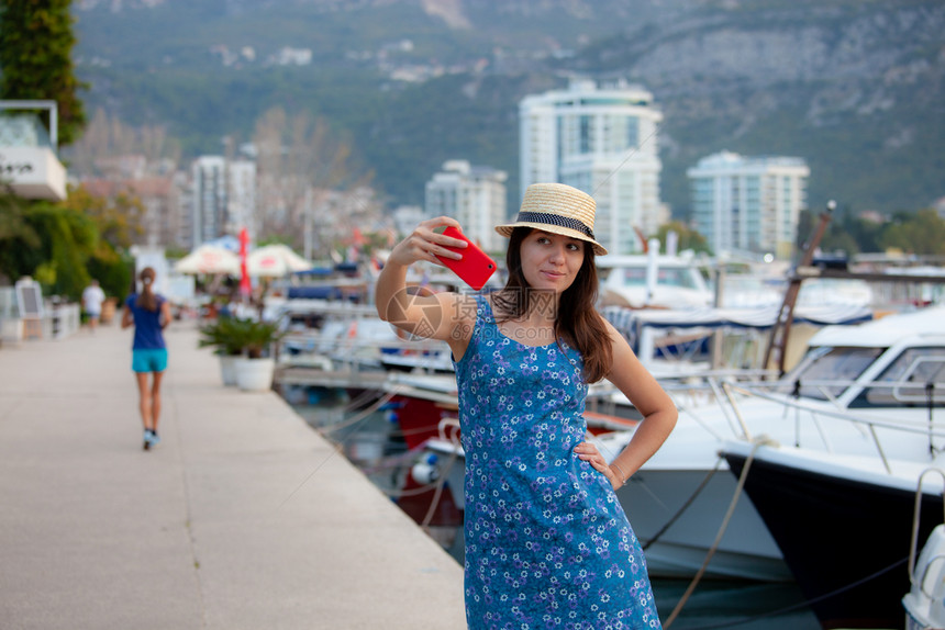戴帽子的年轻旅行女青在夏季阳光明媚的地中海城市拍摄自照片并配有智能手机相布朗特女孩在暑假拍摄照片戴帽子的年轻旅行女青在夏季阳光灿图片