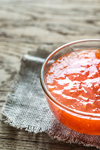 玻璃碗的甜辣椒酱在木背景上图片