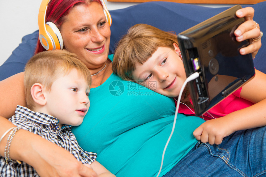 带着耳机的母亲和儿子听音乐在沙发上拥抱着对方图片
