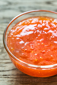 玻璃碗的甜辣椒酱在木背景上图片