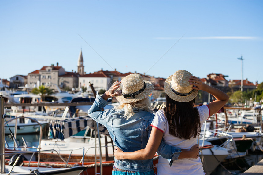 两名观光客的背面望着旧欧洲城市船只码头和度假胜地图片