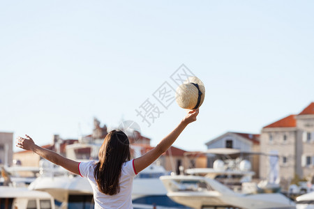 站在地中海城市码头的船靠岸并戴帽子的美丽年轻女图片