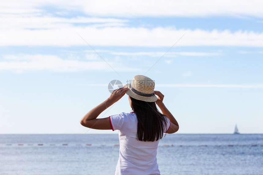 美丽的女孩看着海戴帽子的年轻女孩看着平静的海面图片