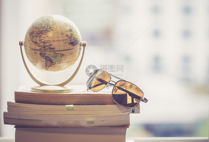 迷你地球模型和太阳镜放在一堆书上用来旅行的标志图片