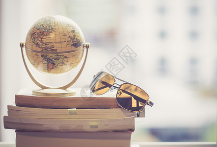 迷你地球模型和太阳镜放在一堆书上用来旅行的标志图片