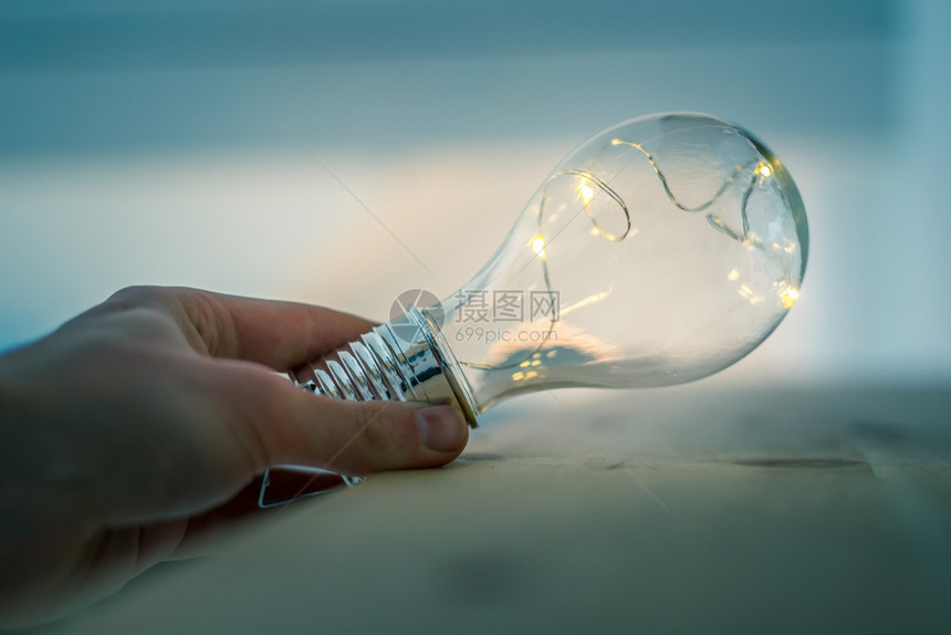 手举着一个LED灯泡在木制地板上有想法和创新的符号窗口图片