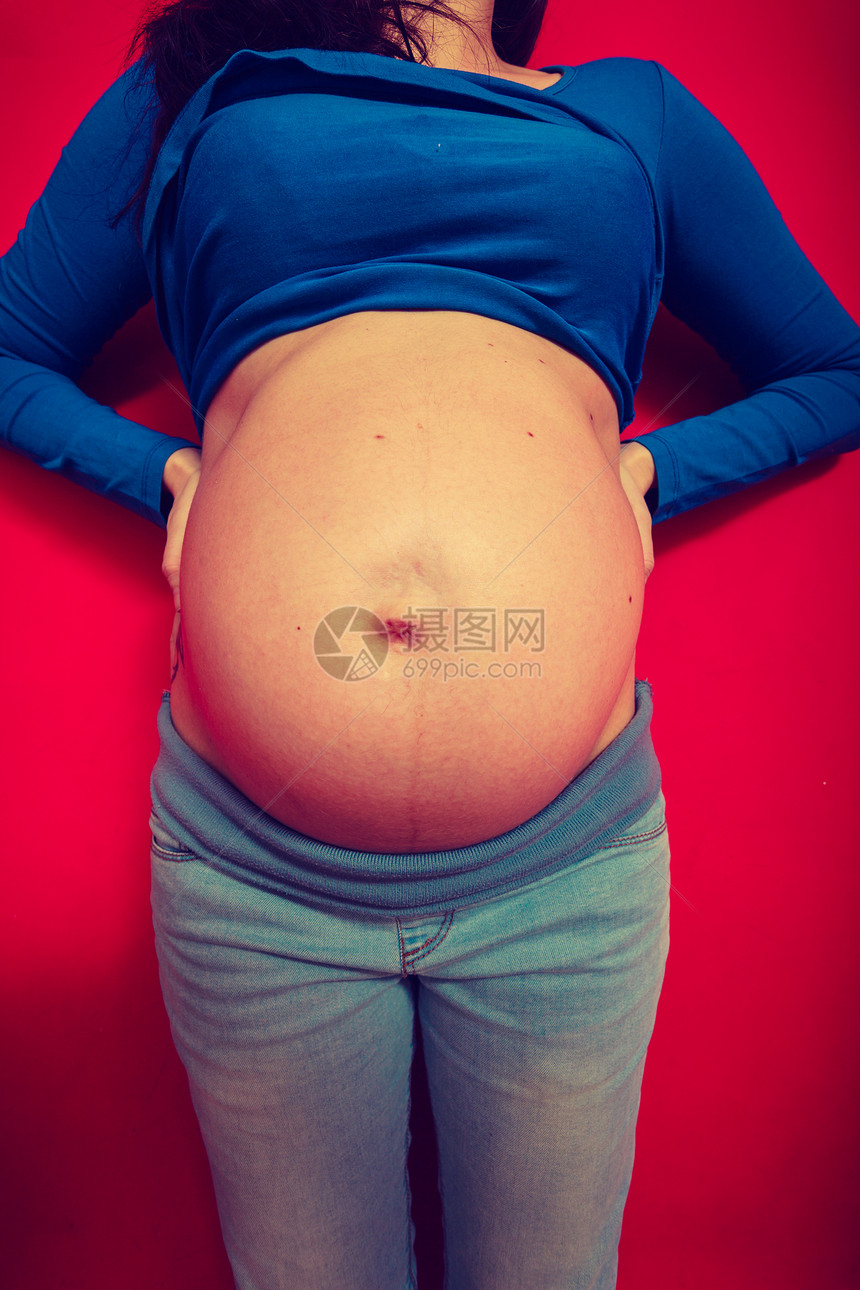 成年妇女展示她的大肚子红背景的室内成年妇女展示她的怀孕肚子图片
