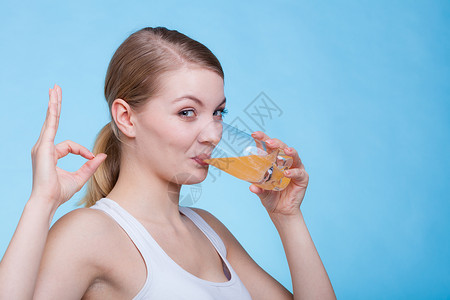 女人拿着橙色的饮料喝着一杯橙色的饮料或果汁工作室拍摄在蓝背景上图片