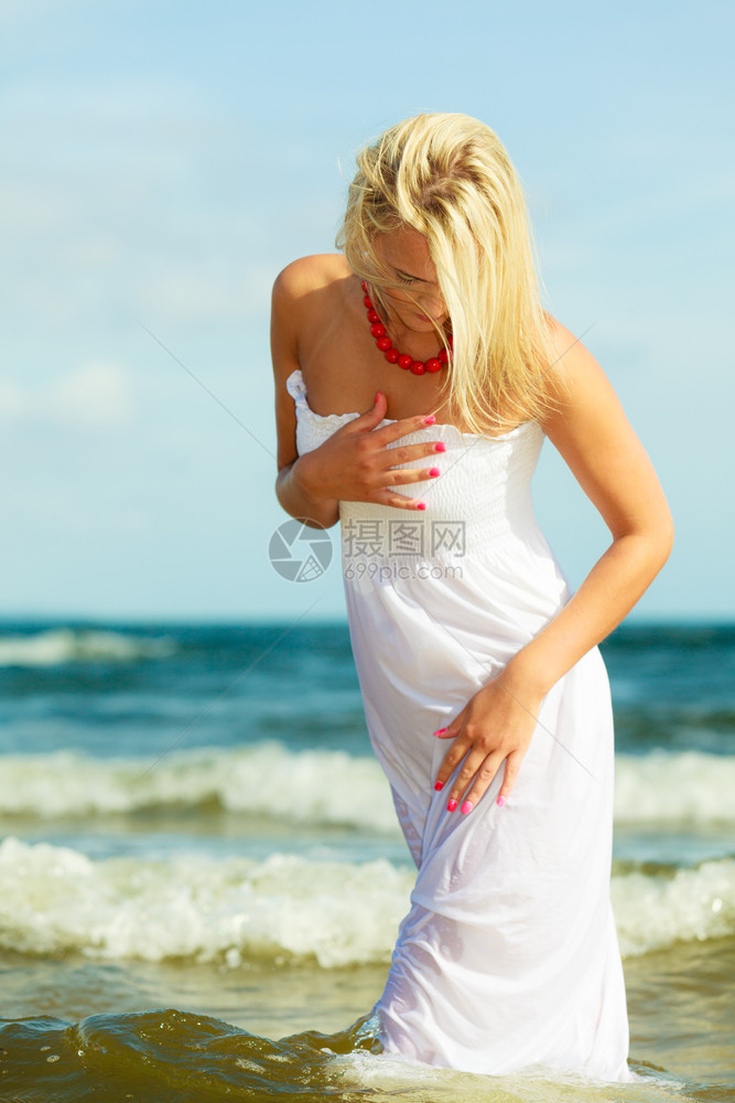 穿着长白色浪漫服装的迷人金发女子在夏天海中漫步图片