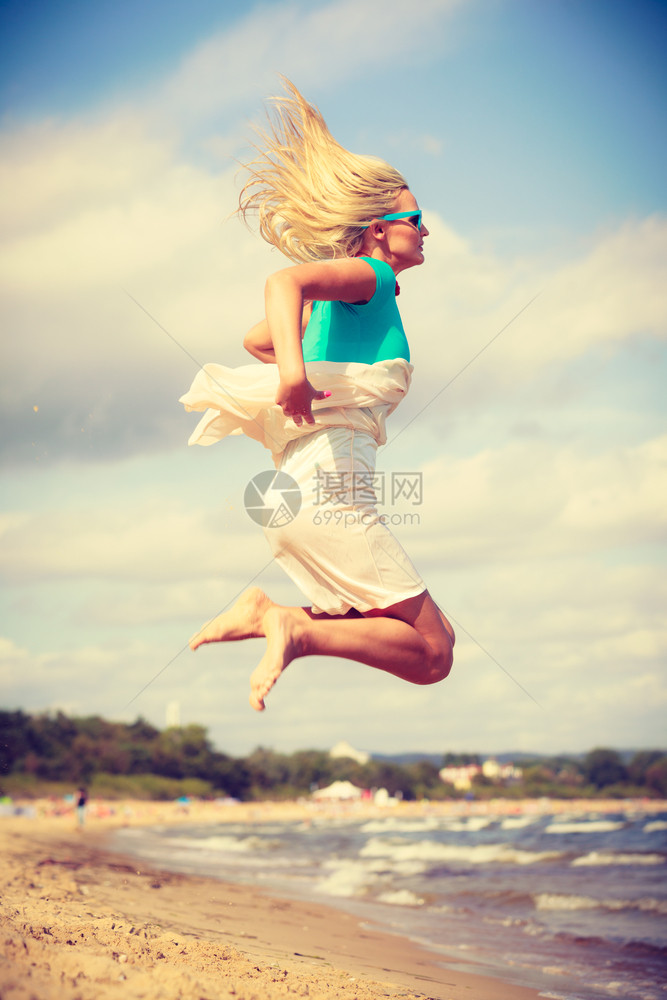 穿着浪漫服装的迷人金发女在沙滩上跳跃夏天放松图片