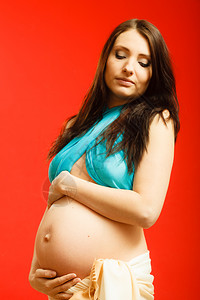 成年妇女展示她的大肚子红背景的室内成年妇女展示她的怀孕肚子图片