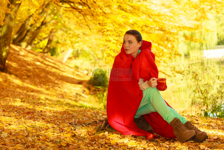 秋天野餐概念在公园或秋天的森林里妇女被红色毯子覆盖在公园或秋天的森林里喝着杯子的热温饮料图片