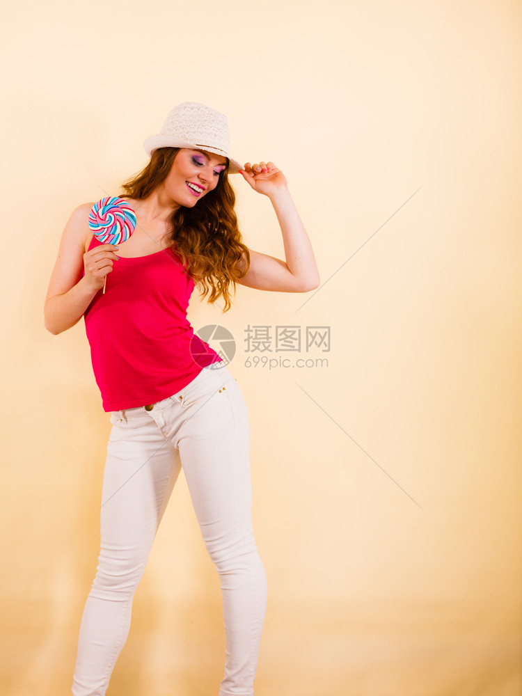 穿着红色T恤的漂亮女人穿着红色T恤暑假帽子手握着大棒糖甜美的食品乐趣概念工作室拍着明亮的蜜蜂女人手里拿着多彩的棒糖图片