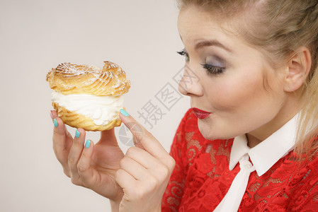 eclair快乐的金发女人拿着美味甜果饼奶油兴奋的面容表情灰色的有趣女人拿着奶油泡芙饼背景