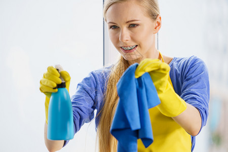 穿着黄色手套的年轻女士在家里用抹布和喷雾洗涤剂擦窗户图片