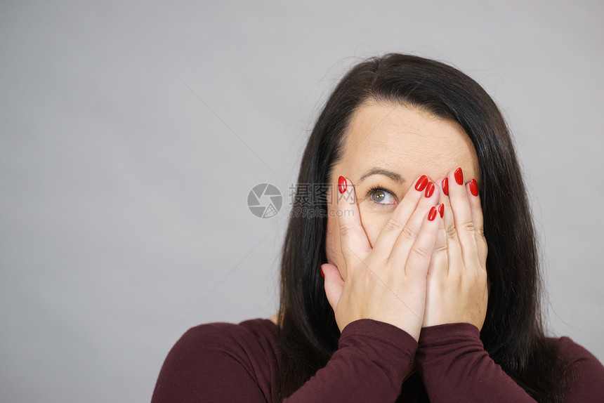 吓得惊的成年妇女通过她的手指偷看双遮面图片