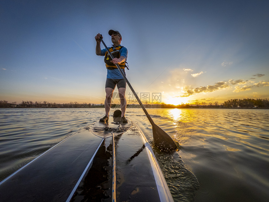 在科罗拉多州一个平静的湖泊上日落时高年体力运动员骑起一个站着的桨板鞠躬风景图片