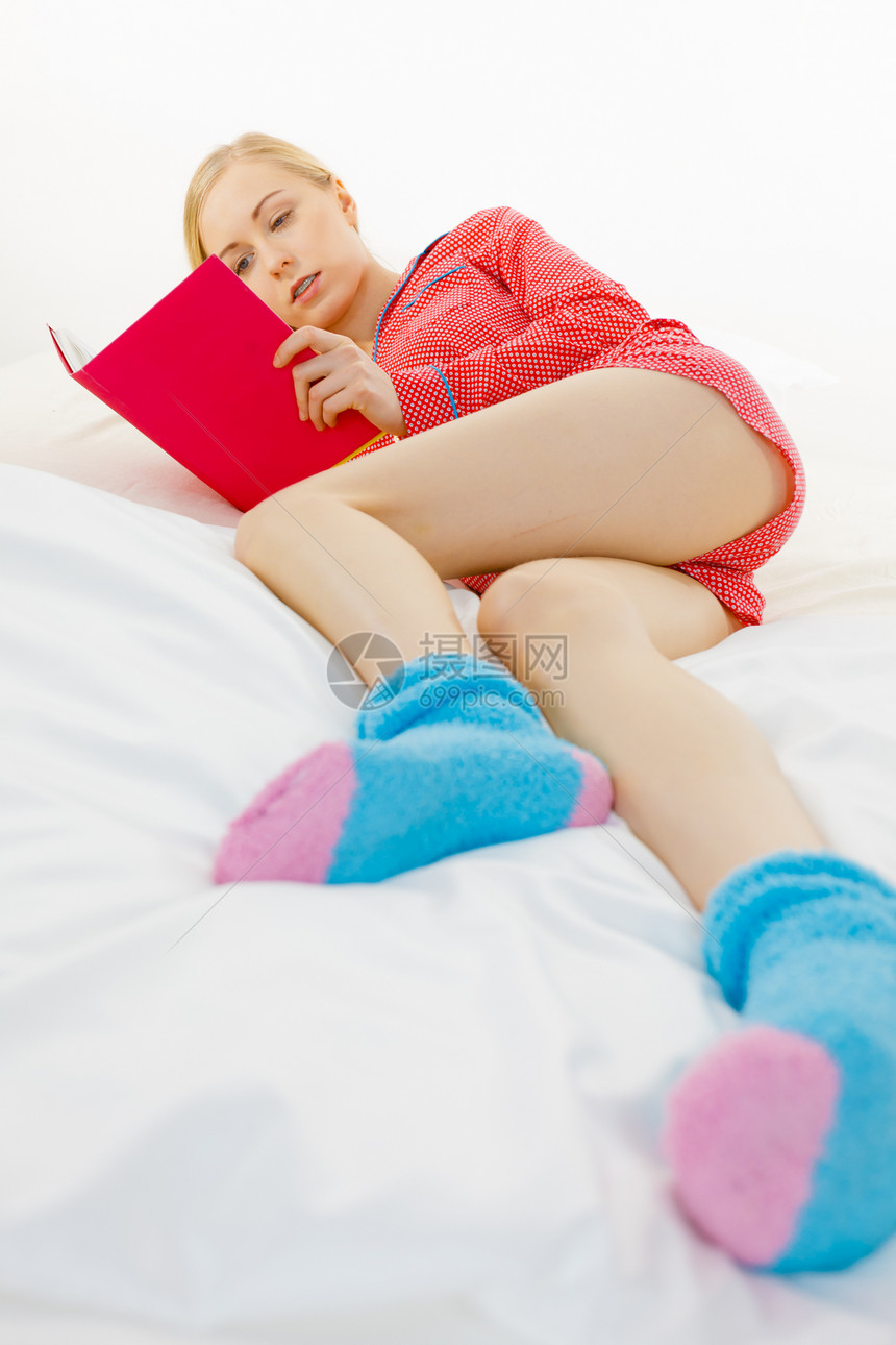 穿着红色圆点睡衣的年轻金发女郎穿着红色圆点睡衣蓝温暖的袜子在家里躺床垫上放松图片