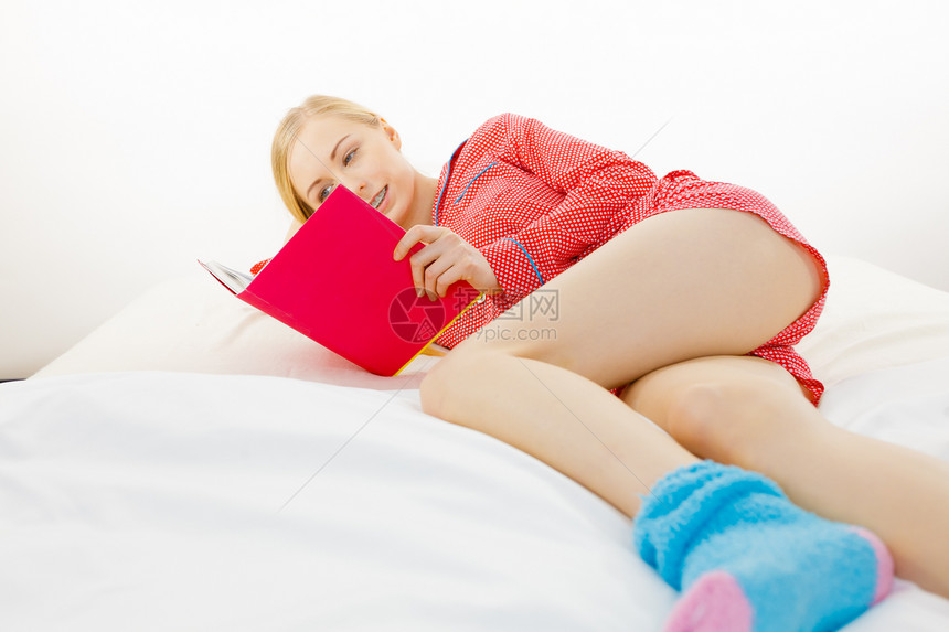 女孩躺在床上阅读书中年轻金发女郎穿着红色圆点睡衣在家中用床垫放松图片