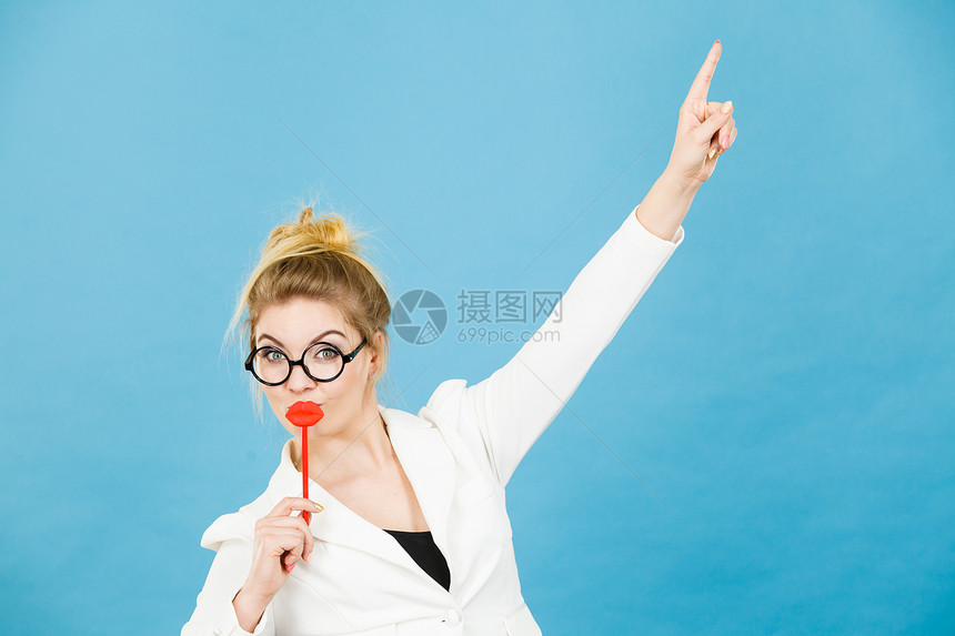 可爱的女商人优雅服装书呆子眼镜戴着红色假嘴唇用棍子玩耍手指向复制空间用蓝色指向复制空间嘉年华有趣的配件概念女人用棍子指向复制空间图片