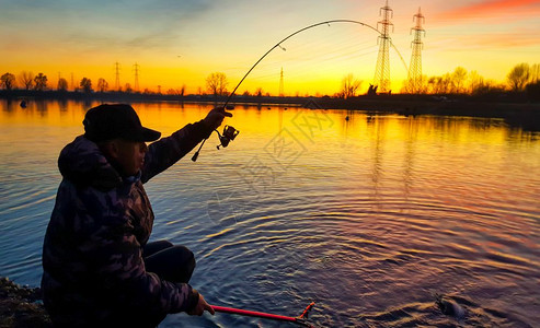 日落时在池塘捕鱼的渔夫图片