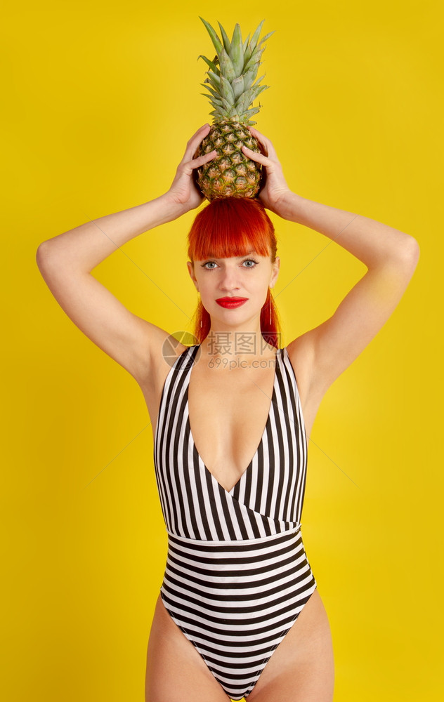 一个穿旧式脱衣泳的年轻女孩头上戴了菠萝背着黄色的亮背景图片