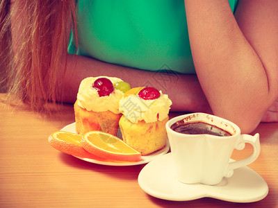有咖啡和美味甜的奶油蛋糕和橙色的女子坐在厨房的可爱女孩喝着热饮吃早餐图片