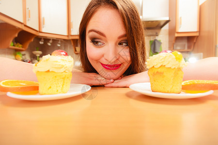 女人看着美味的蛋糕上面有甜的奶油和水果喜欢贪食的概念女人看着美味的甜饼背景图片