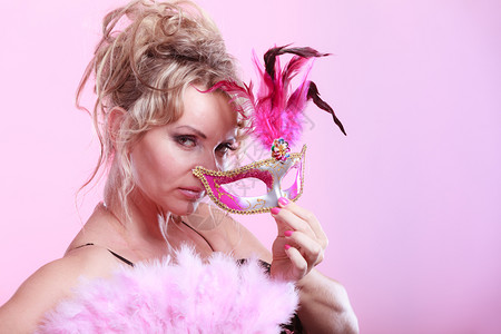 女金色中年模特手握着粉红狂欢节面具彩色背景的羽扇子图片