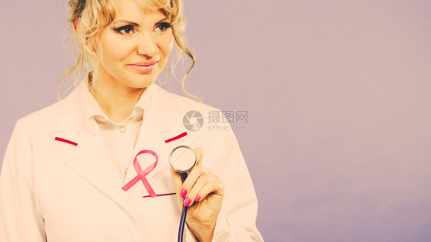 乳癌医疗帮助治概念穿白围裙带粉色丝握有听诊器的女金发医生带粉色癌症丝的医生经过滤带有粉色癌症丝的医生图片