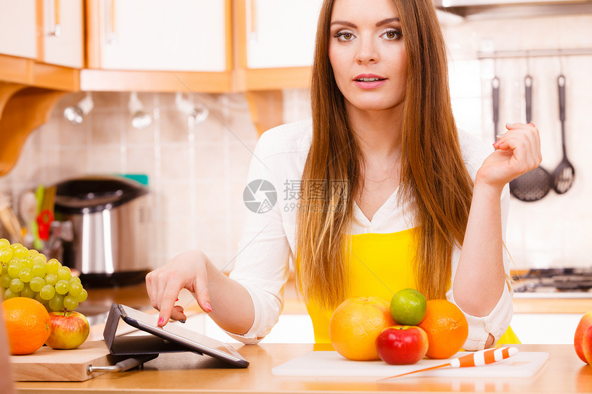 厨房的年轻女家庭主妇许多水果在餐桌上用平板电脑看食谱健康饮烹饪素饮和技术概念图片