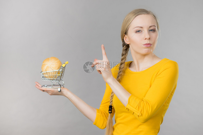 持怀疑态度的妇女持有带面包的购物车轮和面包的购物车图片